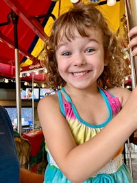 a young girl smiles while standing on a carousel